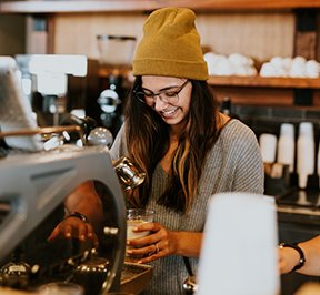 Hipster girl in a yellow beanie making an espresso.