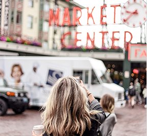 Blonde girl holding coffee in front of Pike Place Market in Seattle.