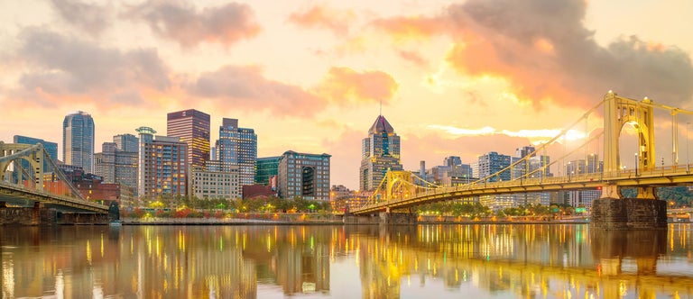 Downtown Pittsburg skyline under a peach sunset. 