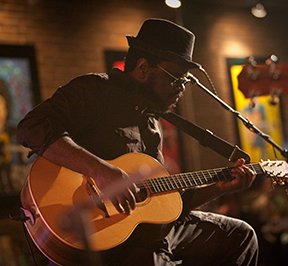 African American musician playing a guitar on a stage.