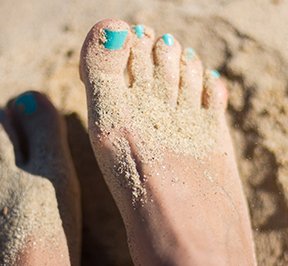 Sandy feet with turquoise toe nails on a beach. 