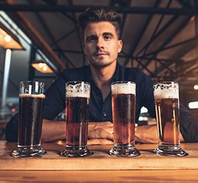 Hipster man sitting behind 4 pint glasses filled with beer.