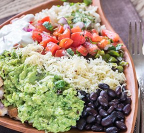 Taco bowl filled with rice, beans, meat and vegetables.