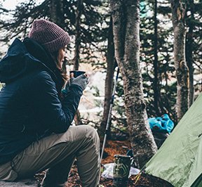 Girl bundled up in warm clothing holding coffee while camping.