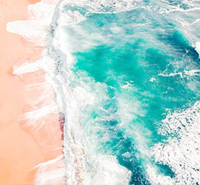 Turquoise ocean water rushing up on peach colored sand. 