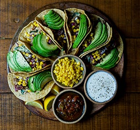 Seven tacos arranged in a circle with salsa, corn and ranch dressing.
