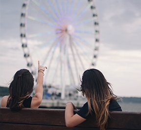 Two young women sitting on a bench in front of the Capital Wheel.
