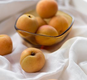 Perfect peaches in a glass bowl sitting on a white, satin table cloth. 