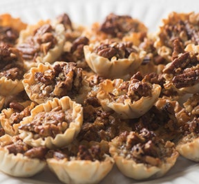 Pecan tassies piled on a white plate.
