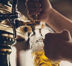 Man pouring a golden beer in a large glass cup.