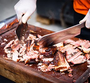 Man cutting up barbecue spit on a butcher block. 