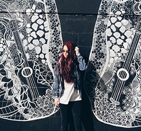 Young girl with red hair standing in front of the Nashville butterfly wing mural. 